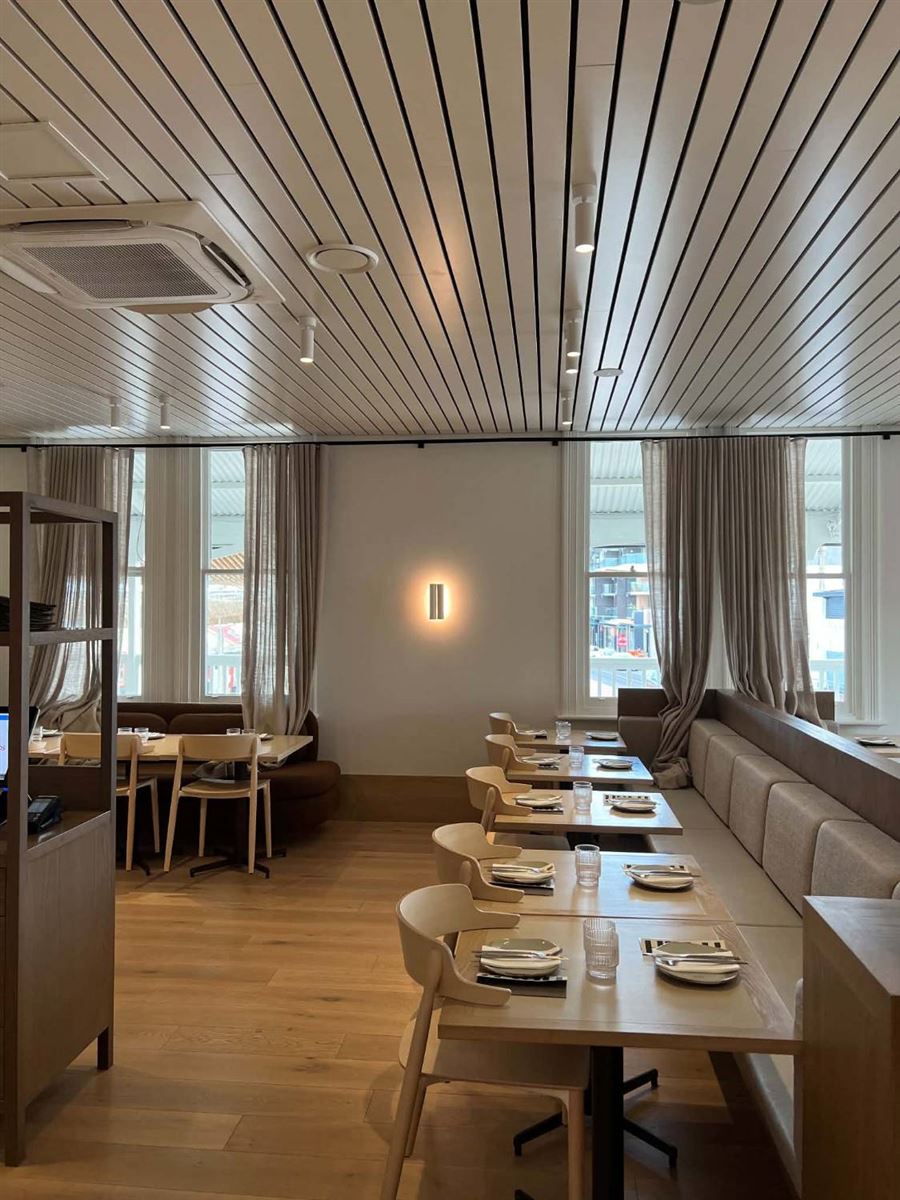 Restaurant dining room with banquette seating, a glowing wall light and spotlights in a timber batten ceiling