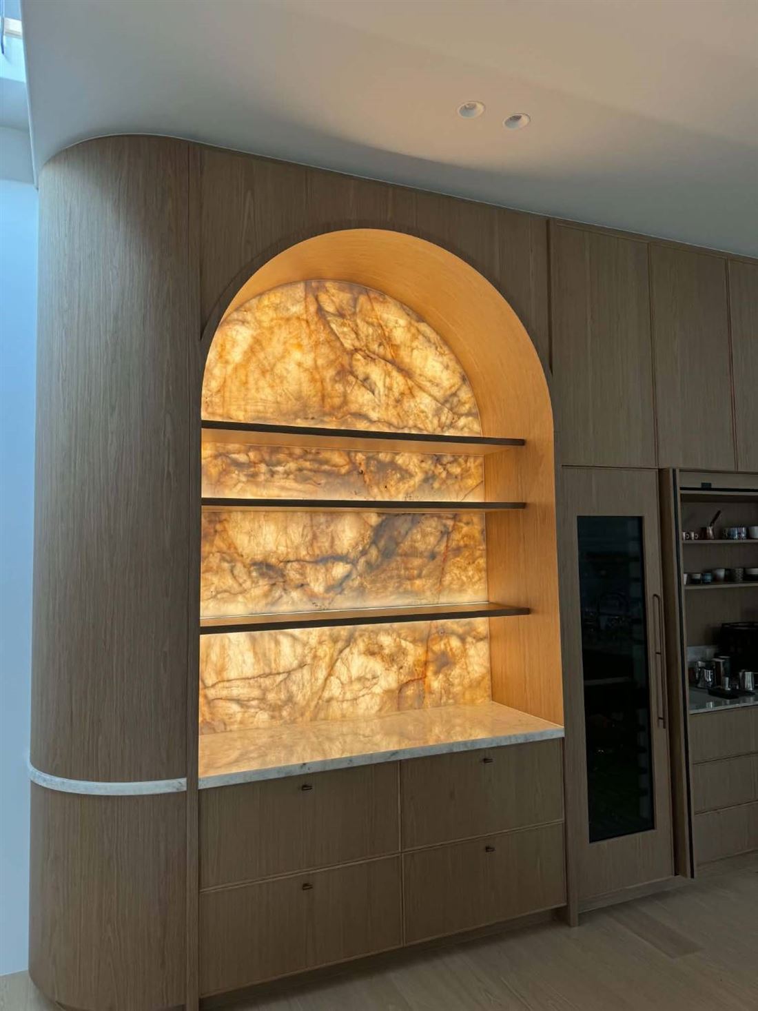 Arched timber joinery with backlit stone panels and lit floating shelves